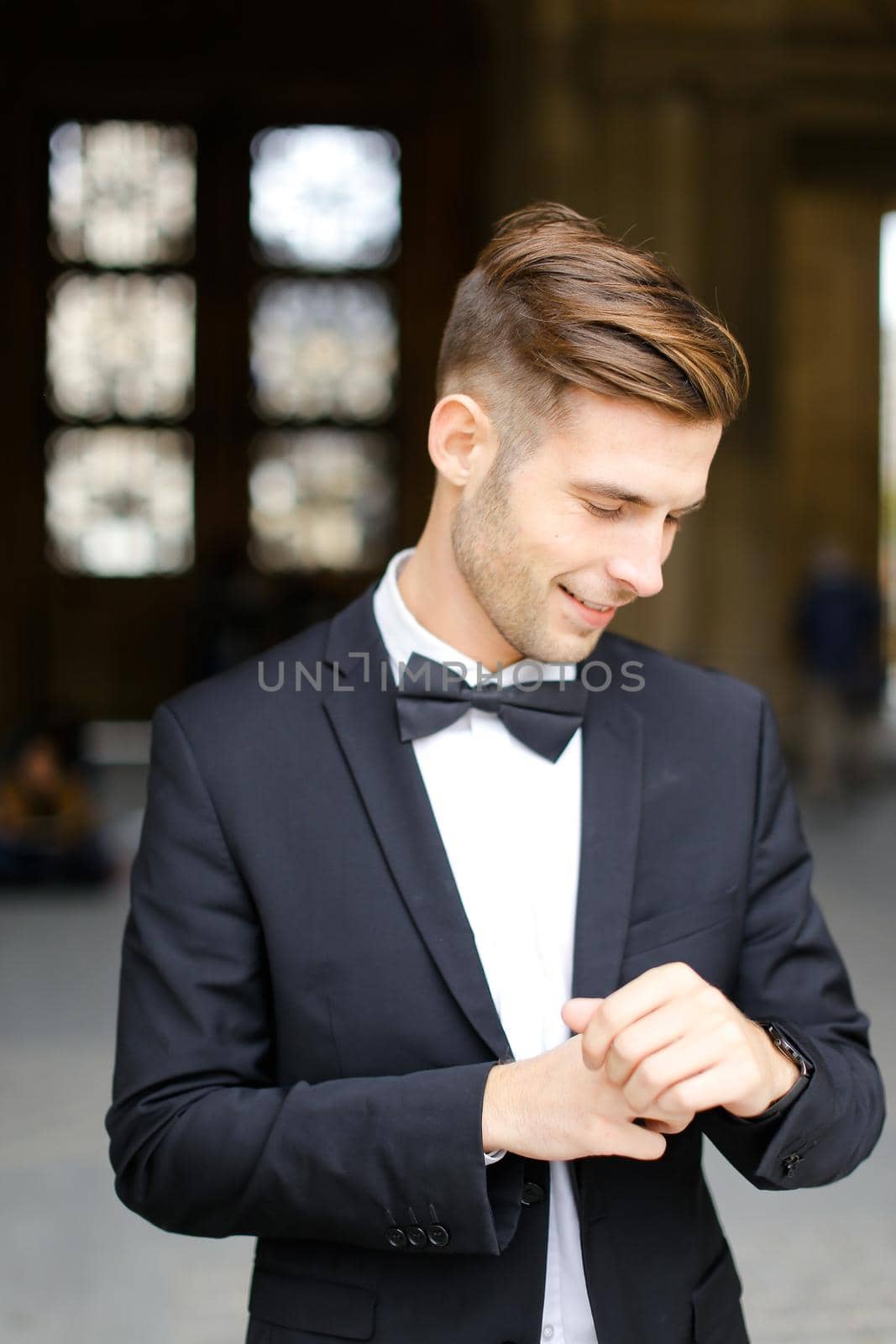 Young groom wearing black suit and waiting, loking at watch. Concept of male model and businessman.