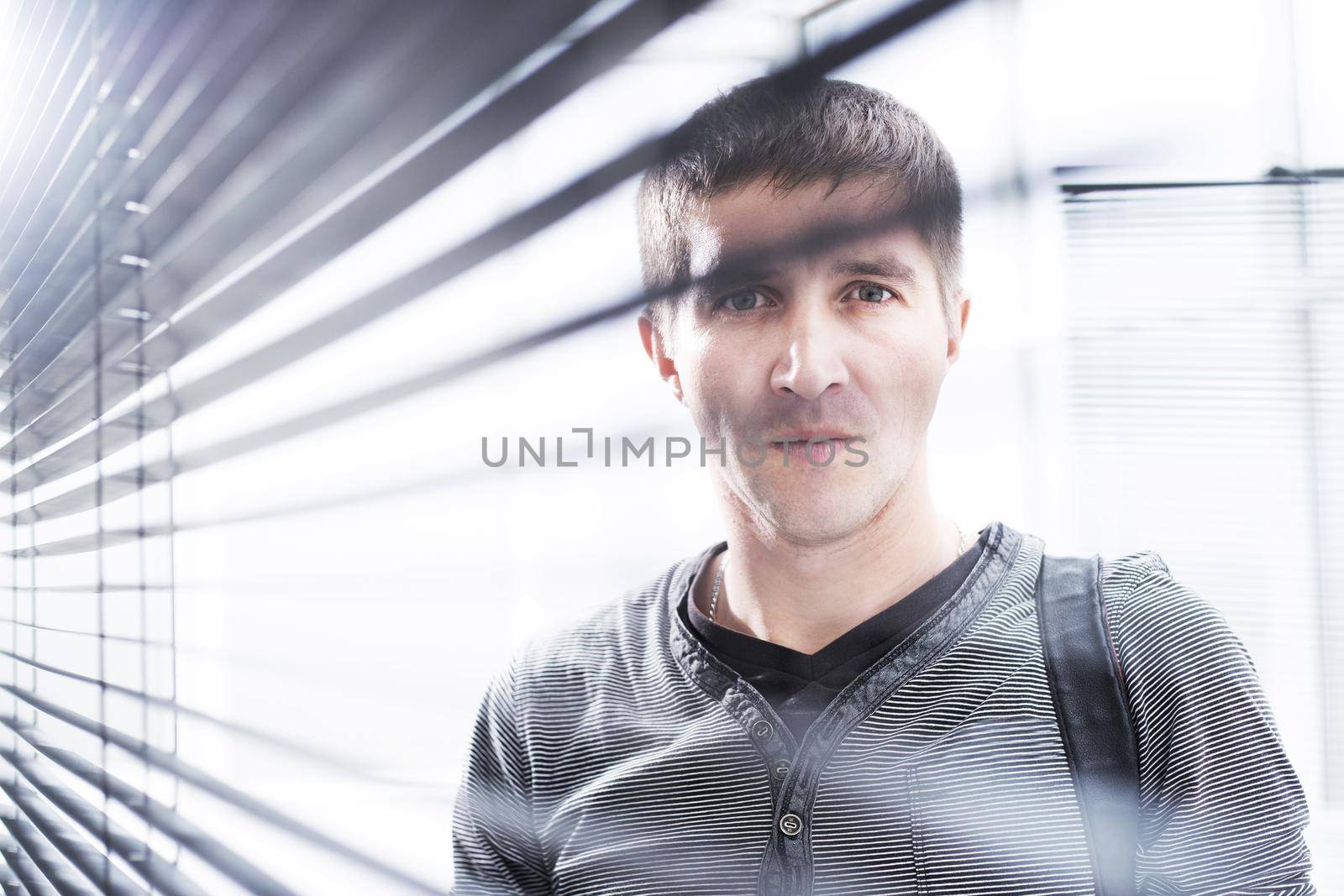 close up. serious young man looking through window blinds
