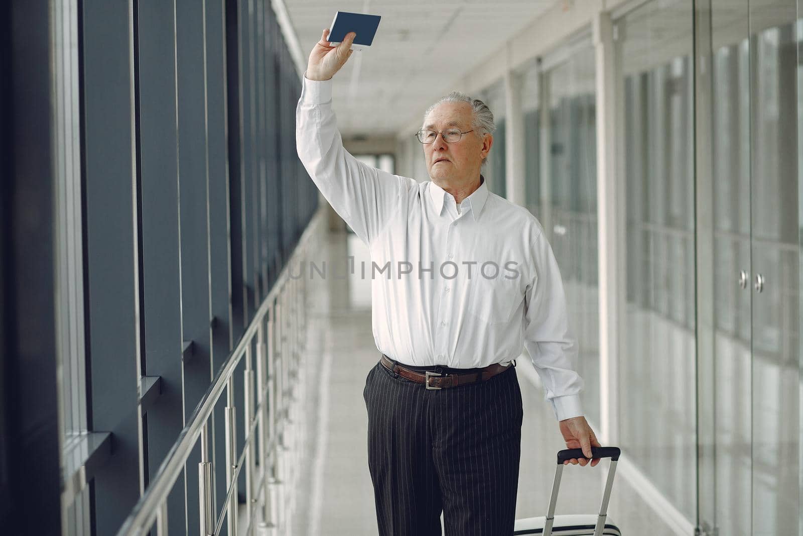 Man at the airport. Senior with suitcase. Male in a white shirt.