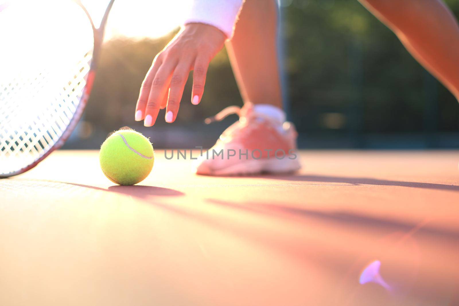 Tennis player raises a tennis ball from the clay court during the game