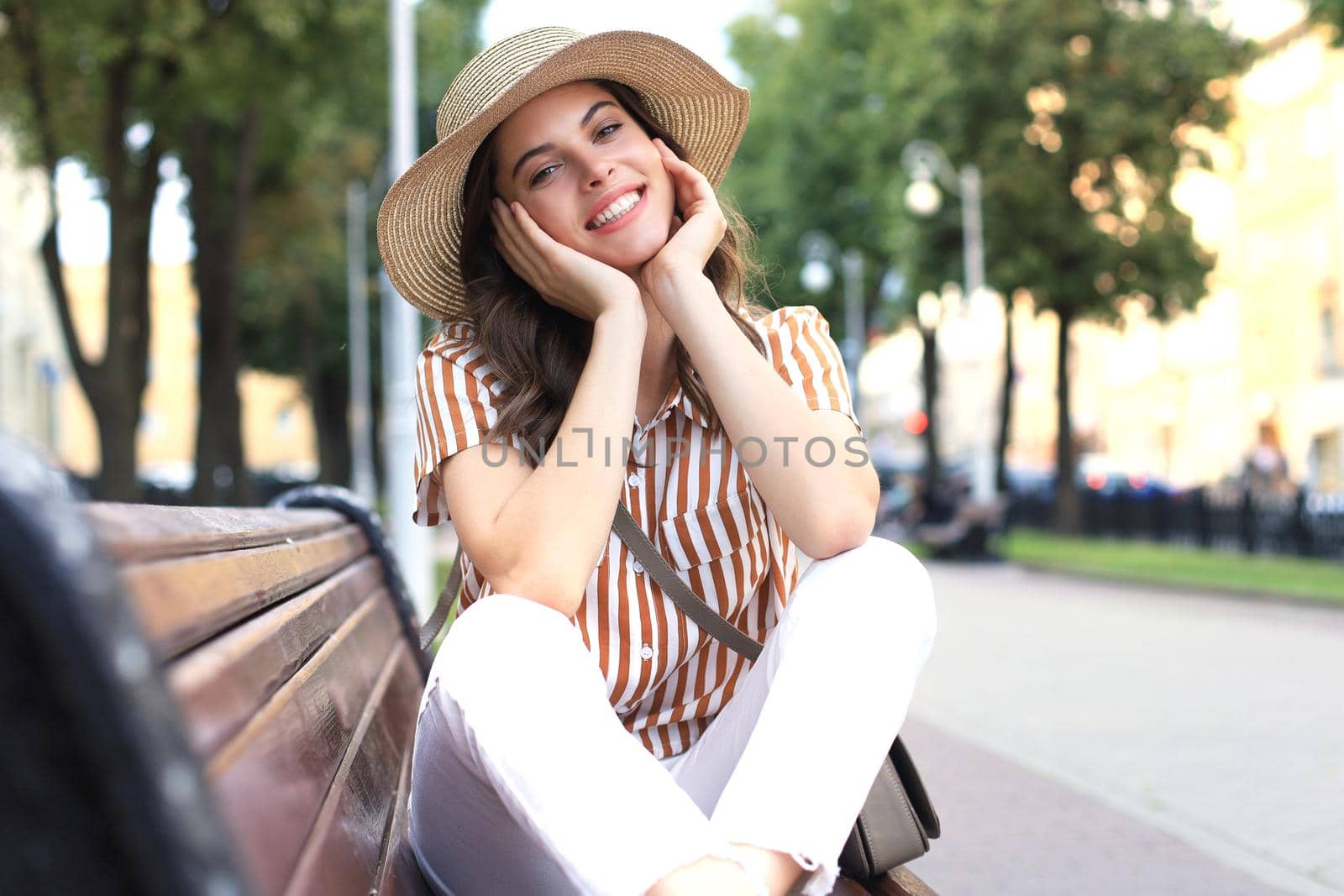 Beautiful smiling young brunette woman sitting on bench in park