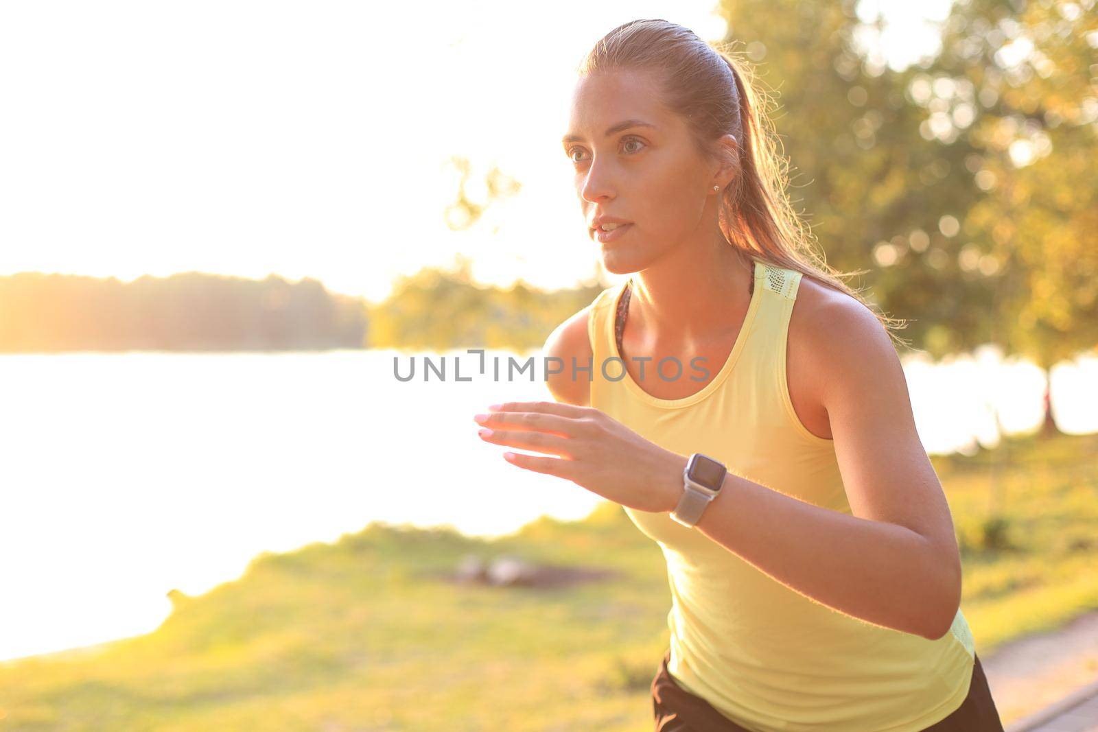 Young woman in sports clothing running while exercising outdoors. by tsyhun