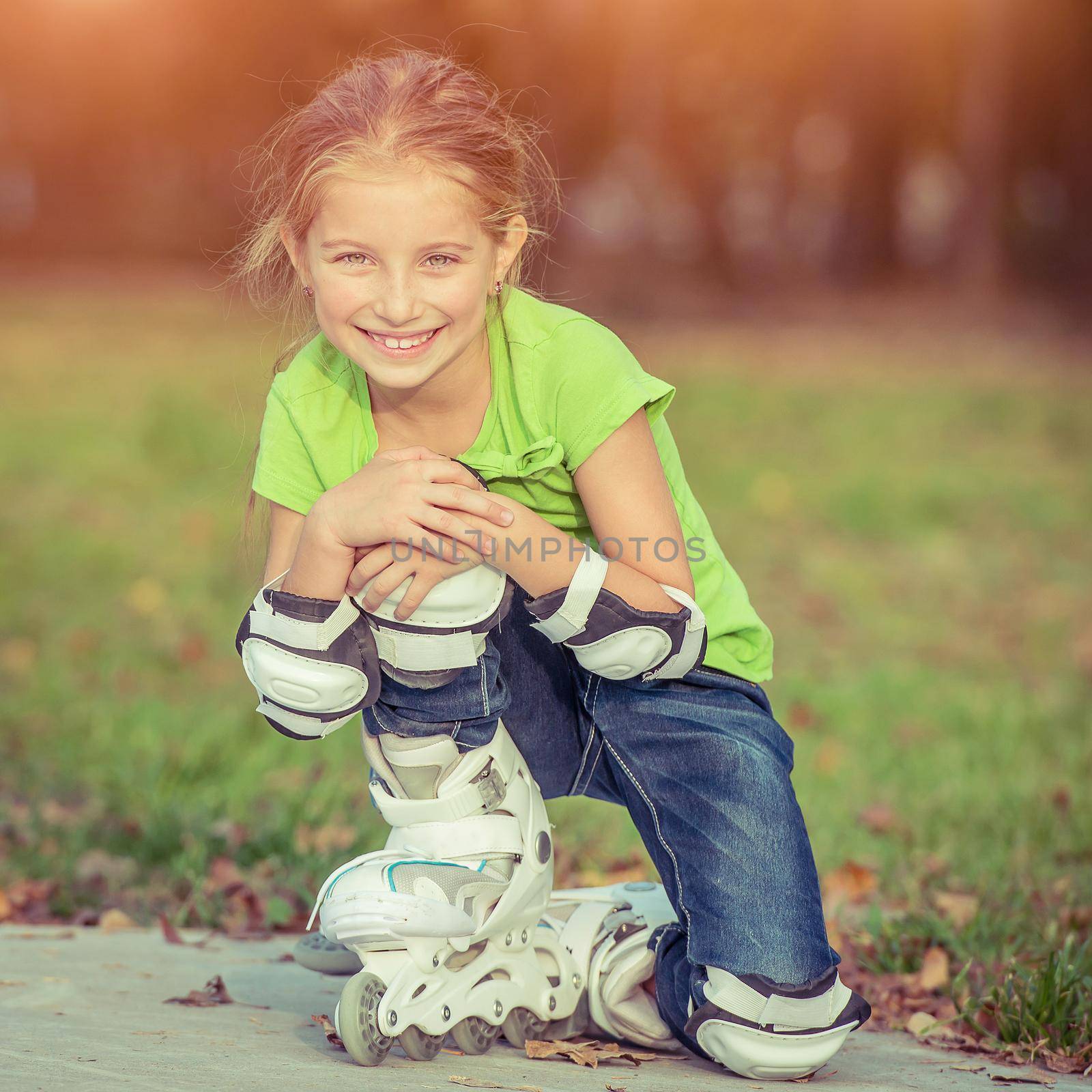 Cute little girl on roller skates sitting in park