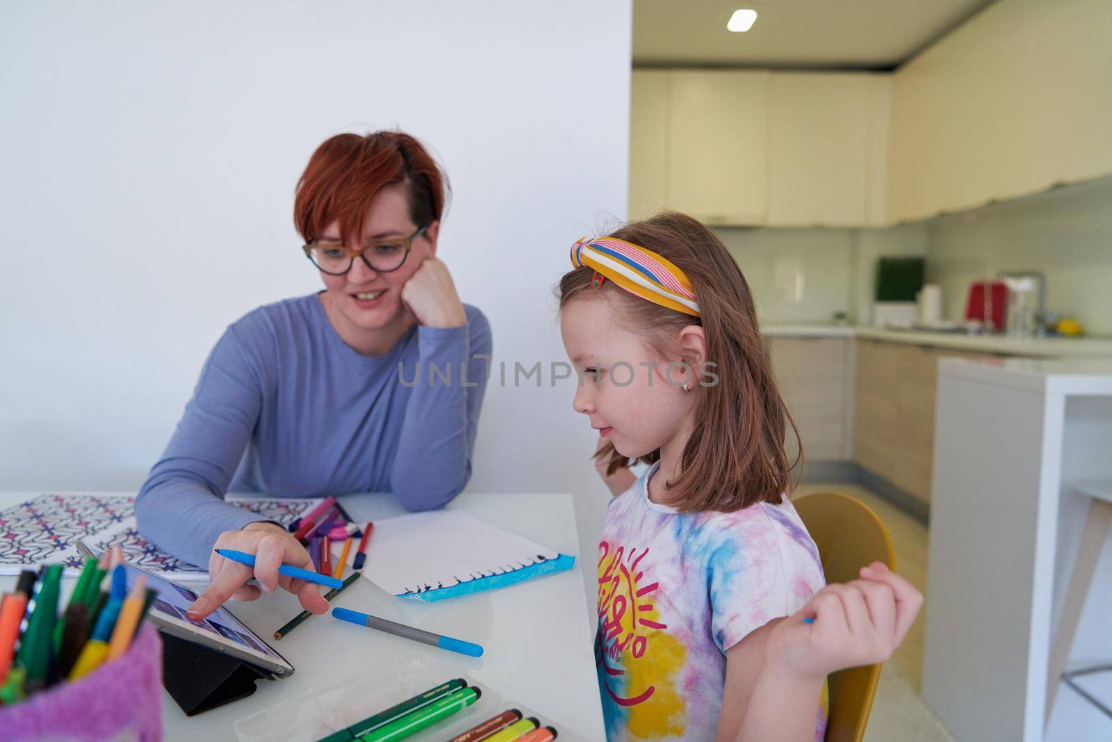 Mother and little daughter  playing together  drawing creative artwork during coronavirus quarantine measuring time on sandglass and listening music on tablet