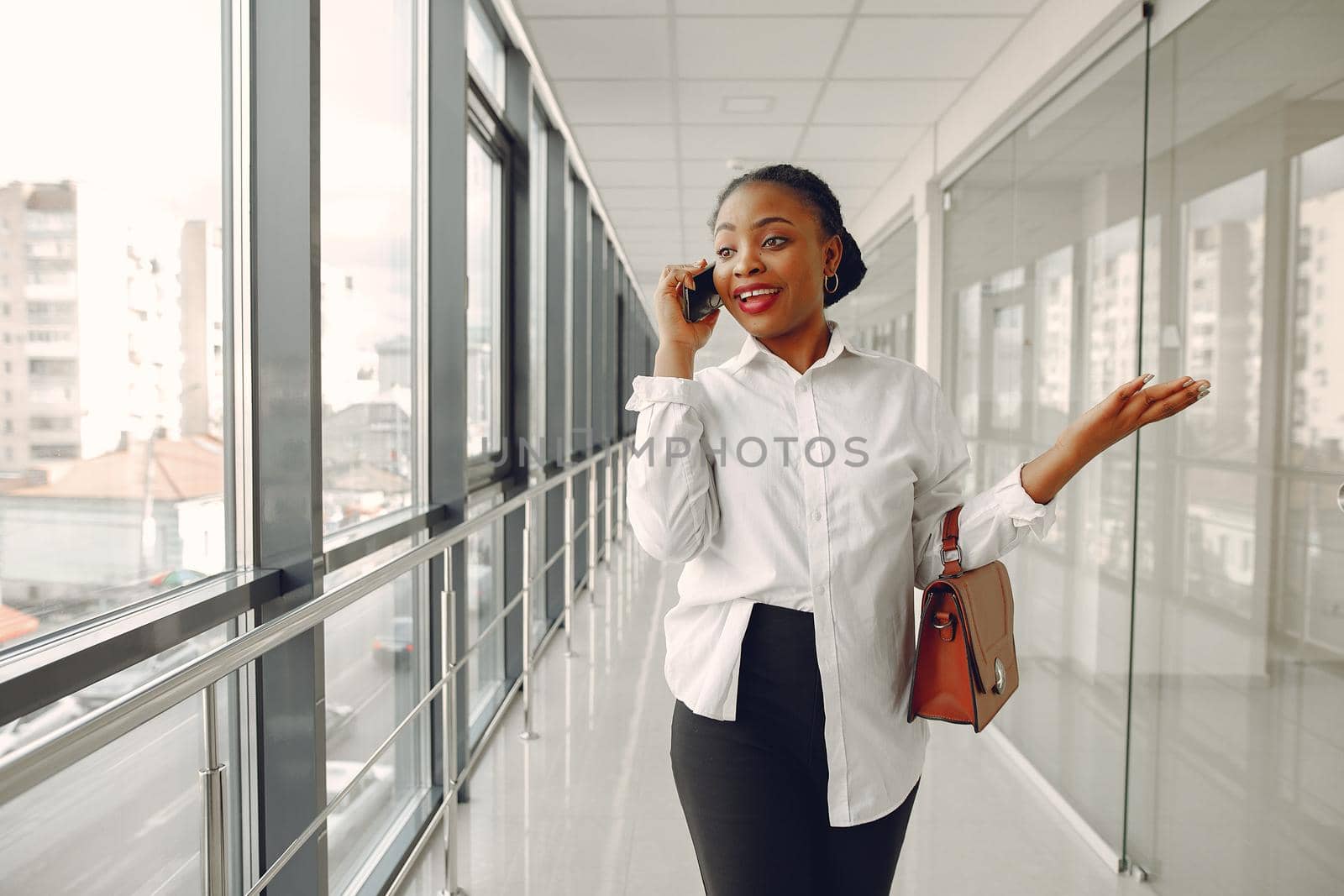 Black girl in the office. Woman in a white shirt. Lady use the phone.