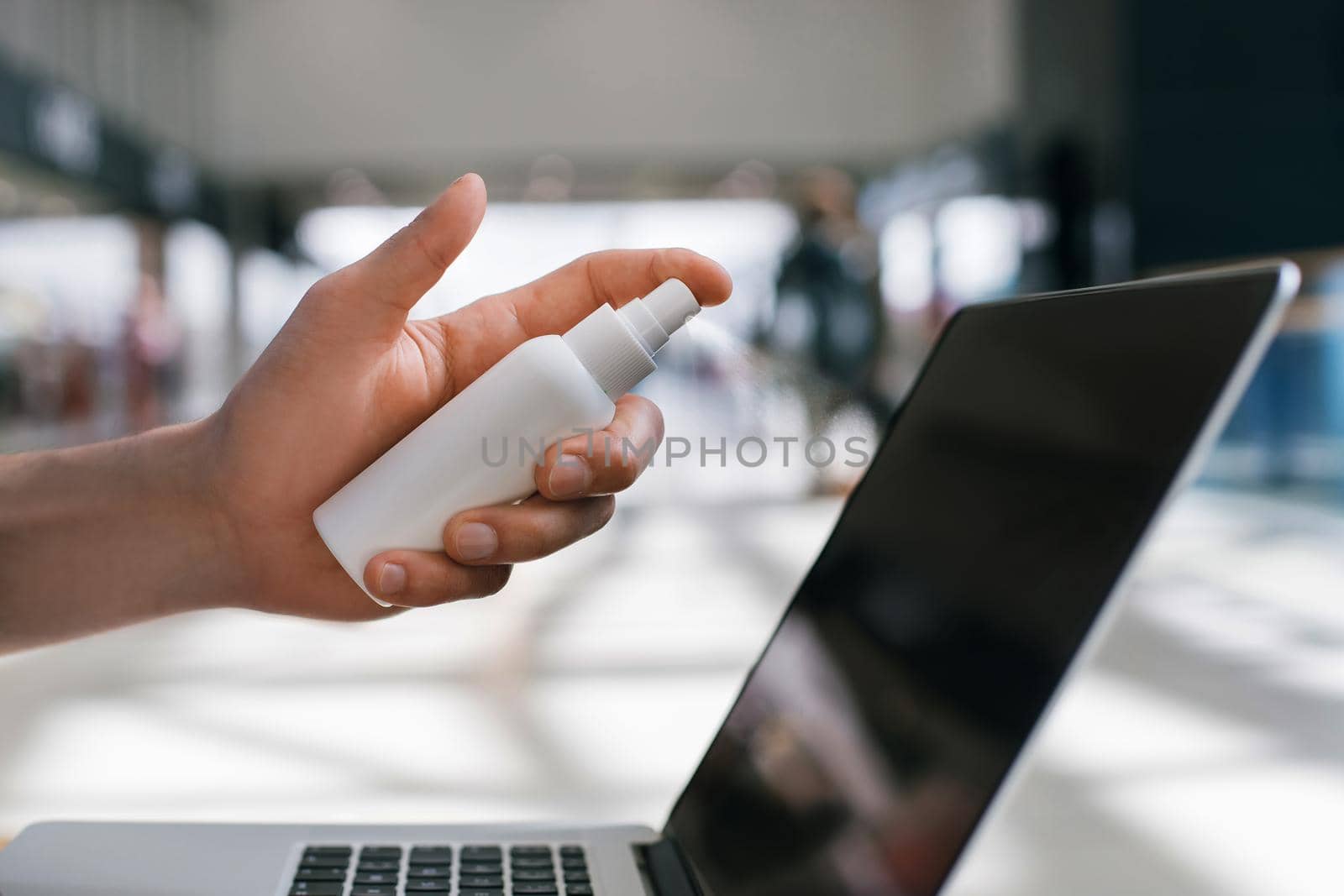 young man decontaminating his laptop with antiseptic. health protection concept