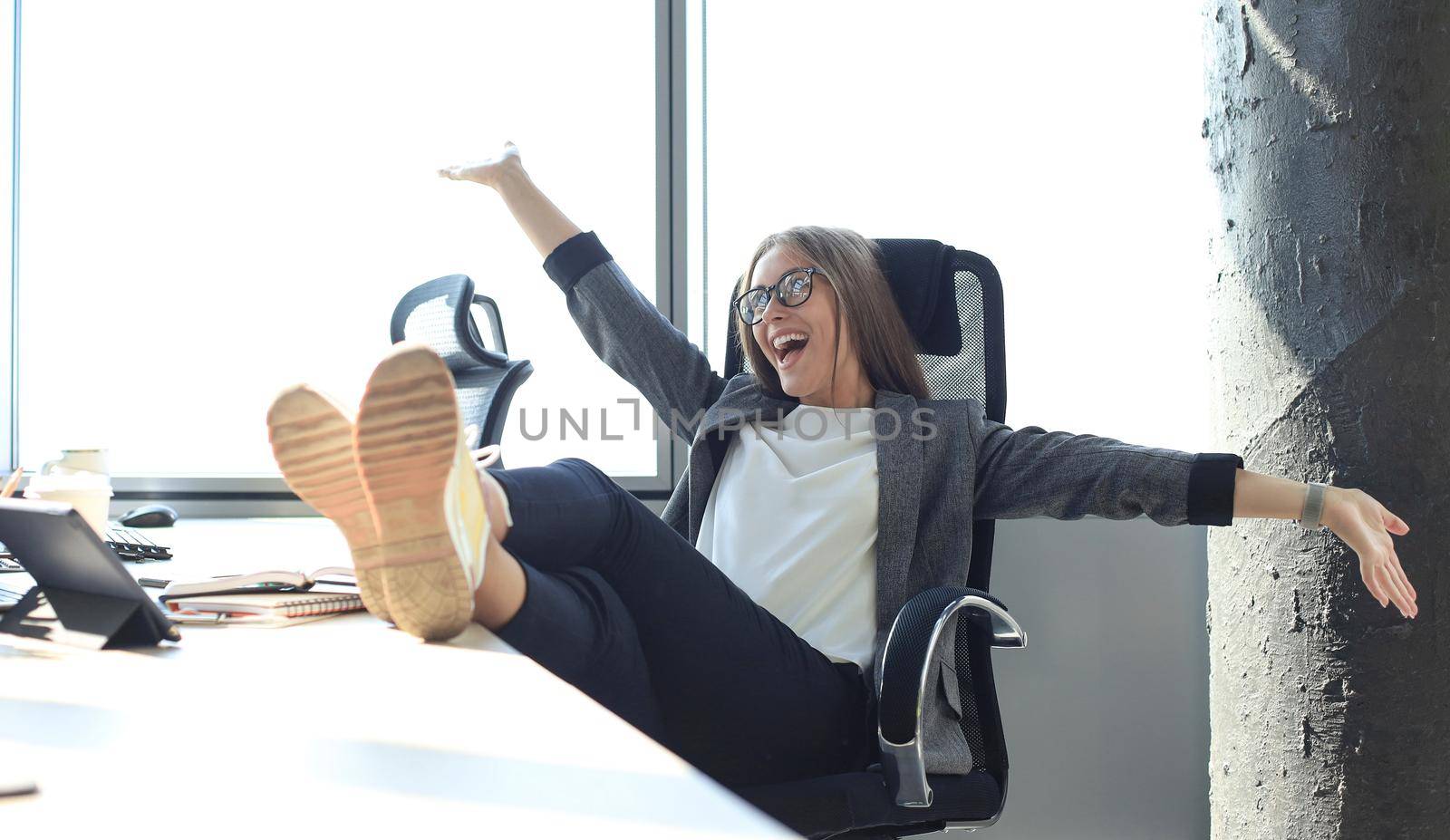 Beautiful business woman is celebrating triumph in business deal at office with hands up. Business lady is relaxing in office