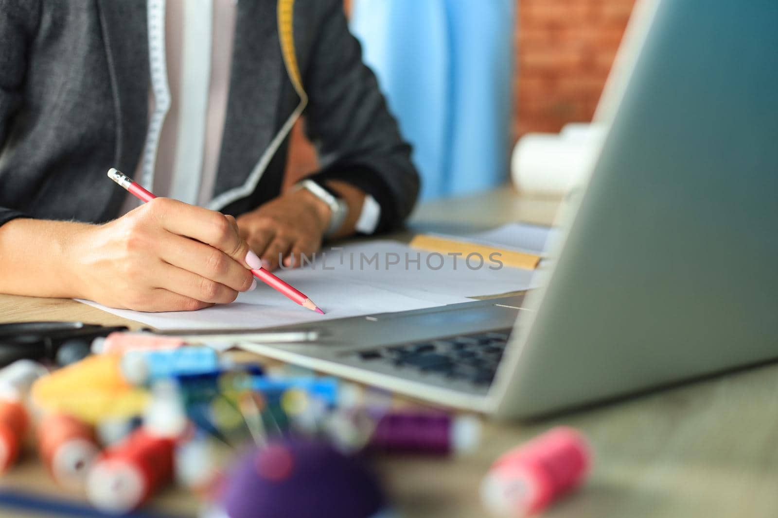 Cropped shot of stylish fashion designer working with laptop and drawing sketch in atelier