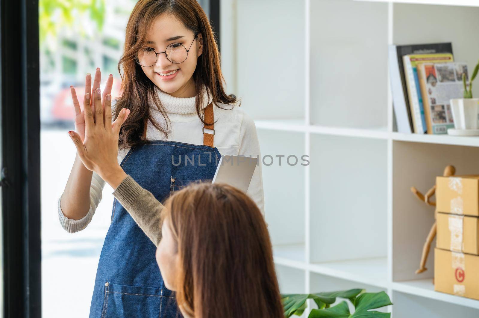 Sell products to business owners online. Focus on the face of a woman in white expressing joy to a friend whose online sales exceeded their expectations