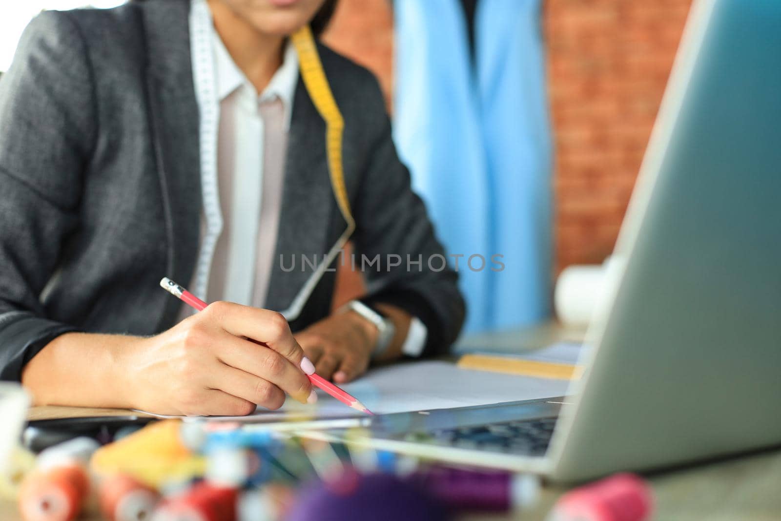 Cropped shot of stylish fashion designer working with laptop and drawing sketch in atelier