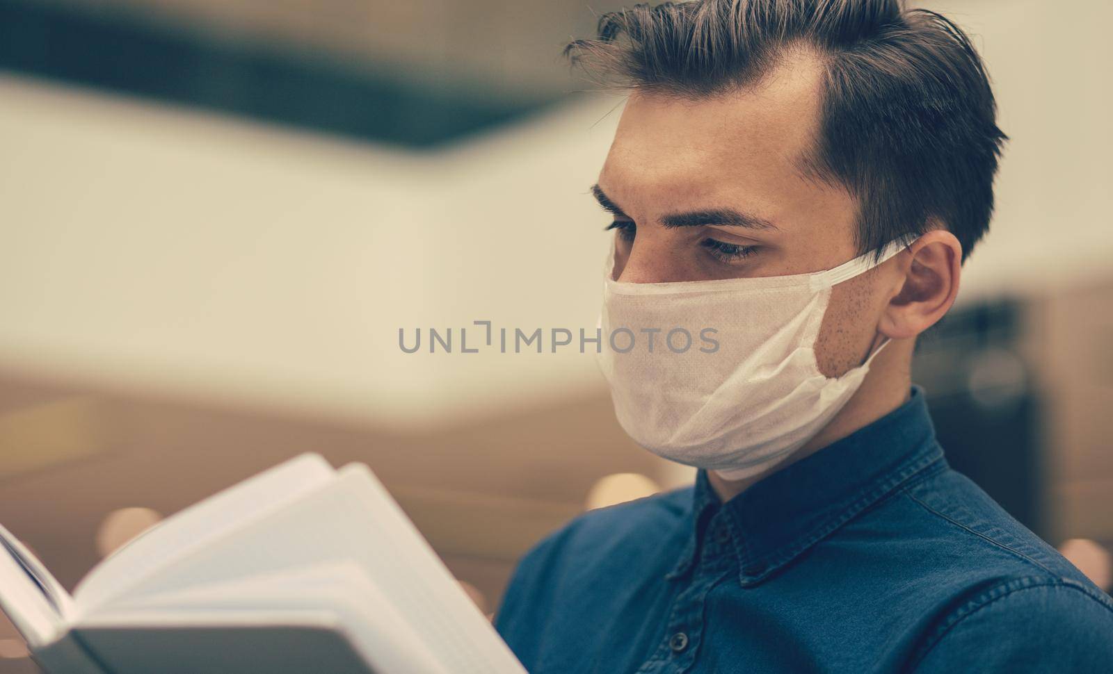 young man reading a book sitting at a table in the food court by SmartPhotoLab