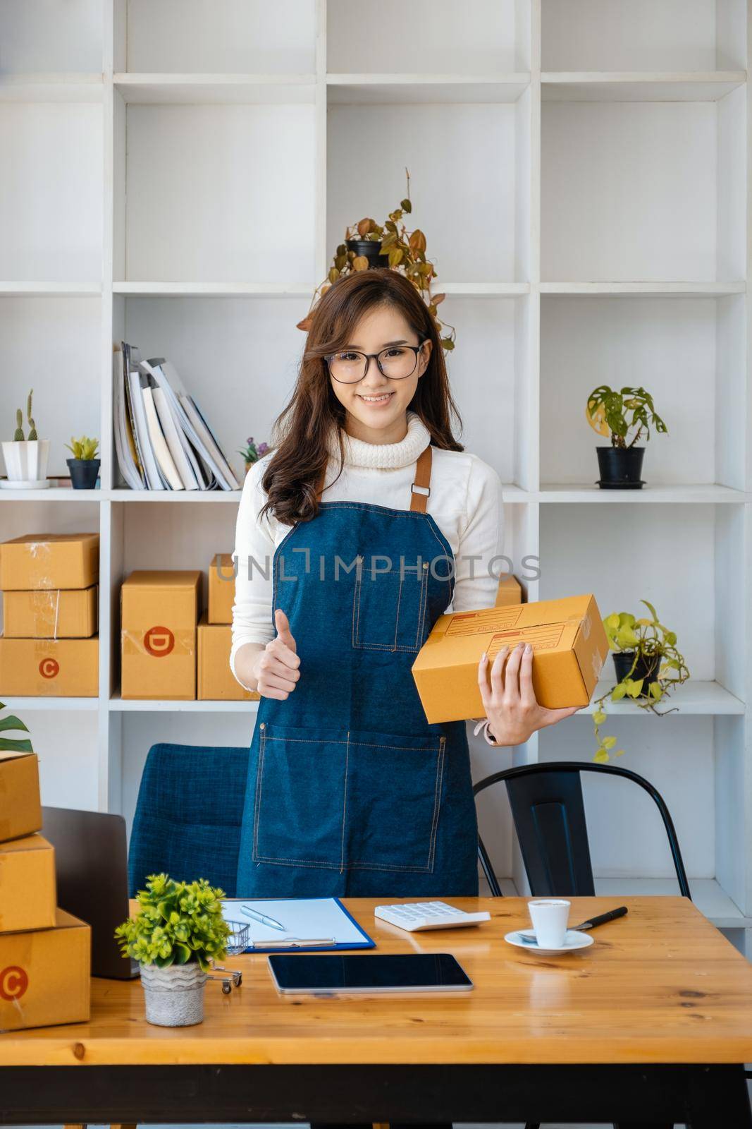 Business owner picking up parcel boxes And use a computer to check online orders to prepare the packaging. pack products to send to customers. by Manastrong