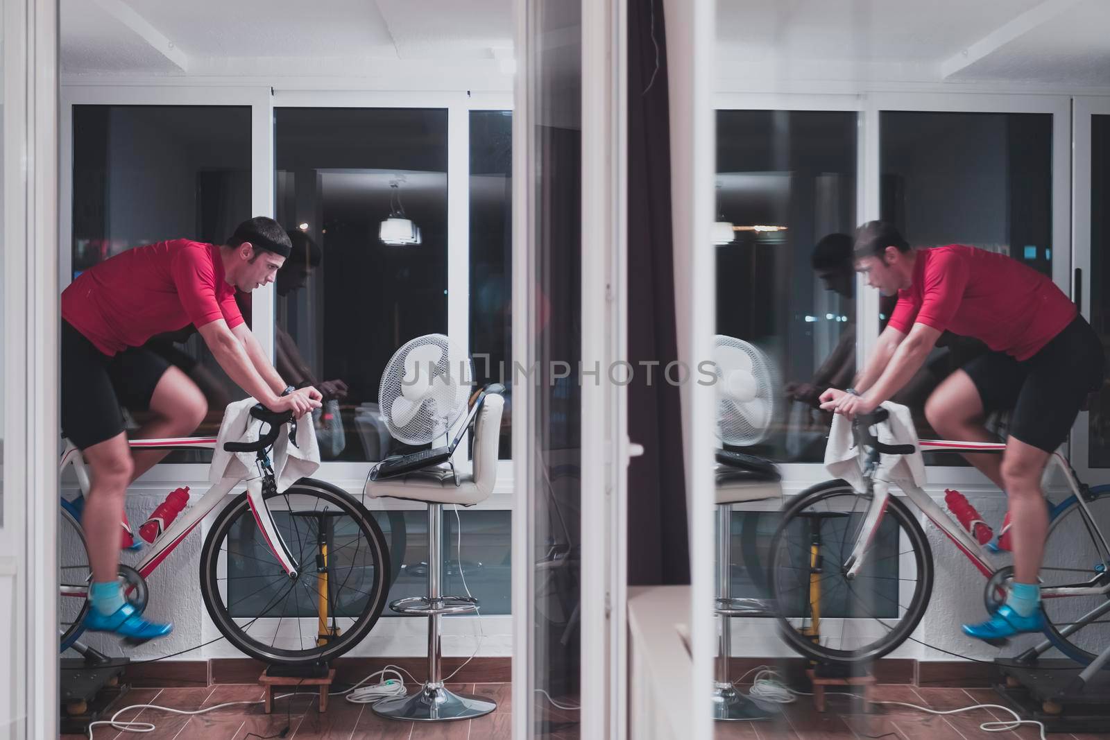 Man cycling on the machine trainer he is exercising in the home at night playing online bike racing game by dotshock