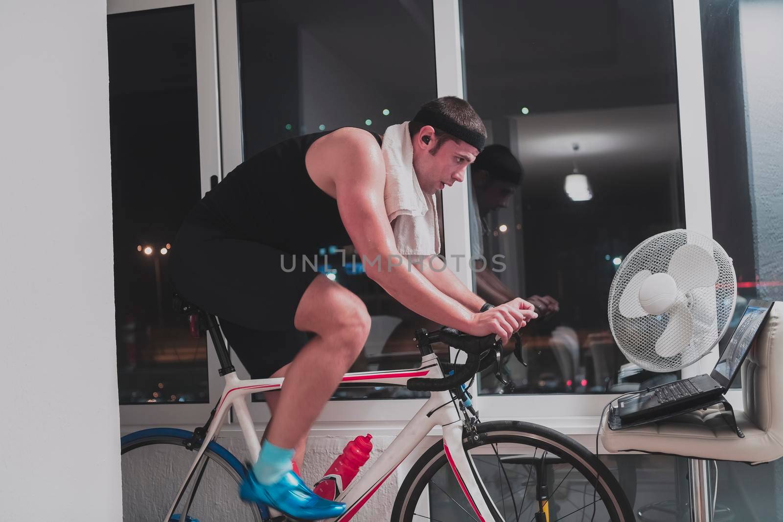 Man cycling on the machine trainer he is exercising in the home at night playing online bike racing game by dotshock