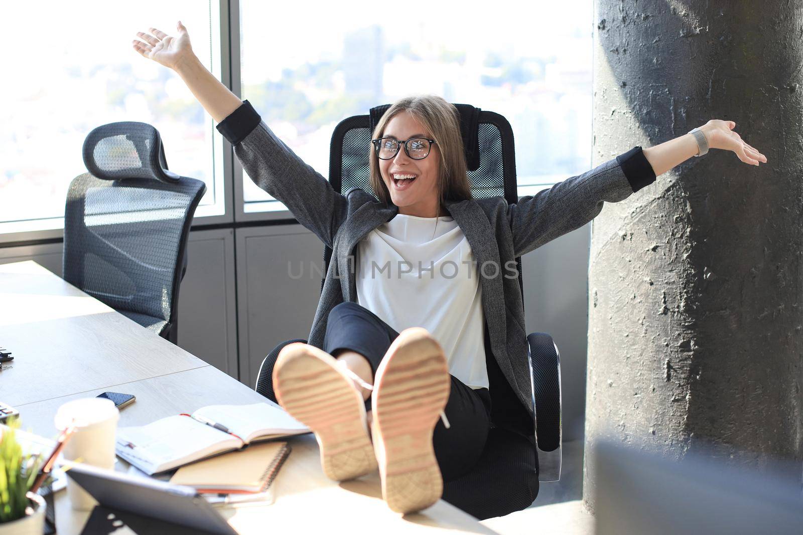 Beautiful business woman is celebrating triumph in business deal at office with hands up