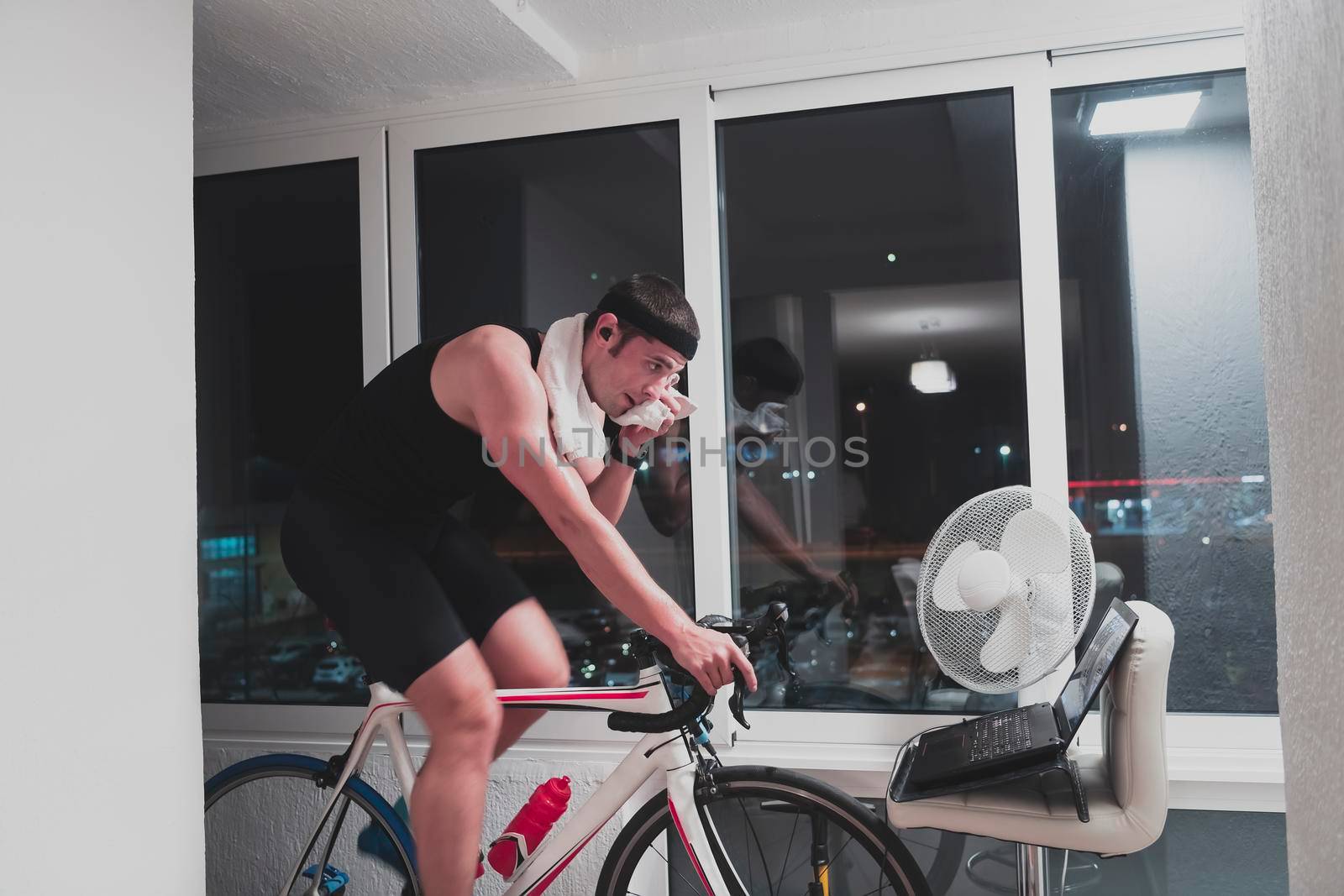 Man cycling on the machine trainer he is exercising in the home at night playing online bike racing game by dotshock