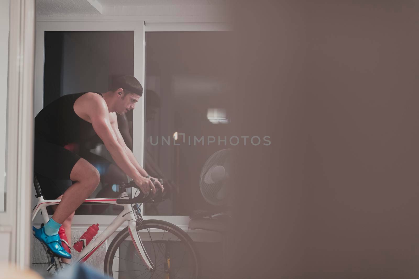 Man cycling on the machine trainer he is exercising in the home at night playing online bike racing game by dotshock