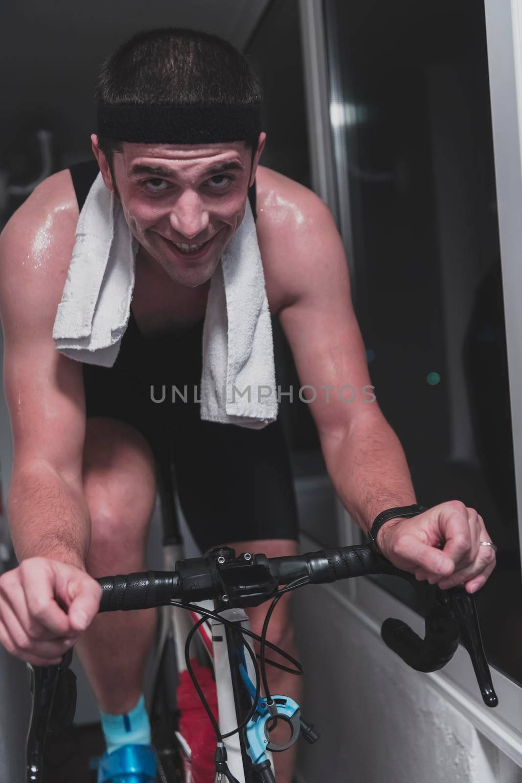 Man cycling on the machine trainer he is exercising in the home at night. Playing online bike racing game during coronavirus covid19 lockdown. New normal concept.