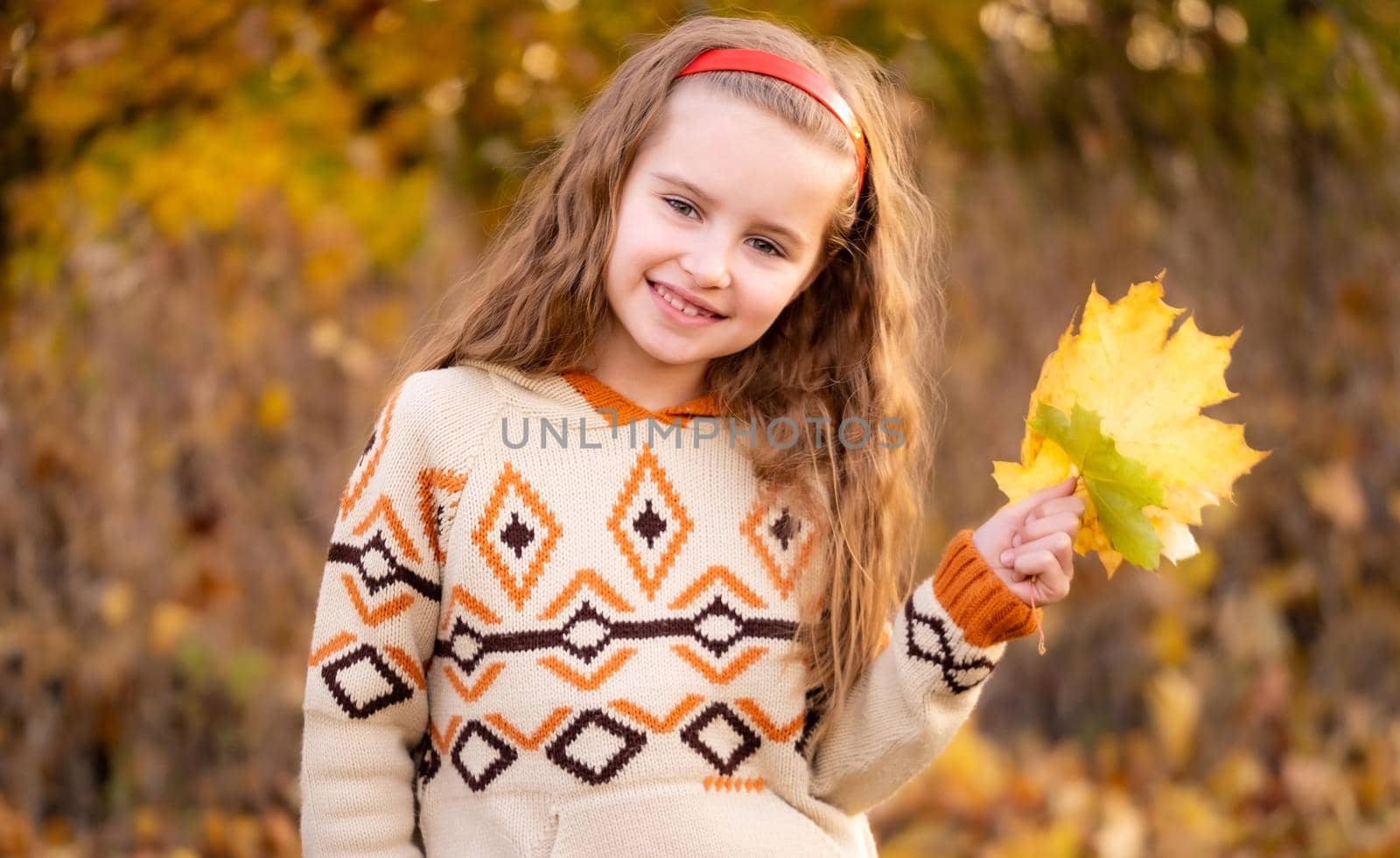 Nice little girl holding autumn leaves outdoors
