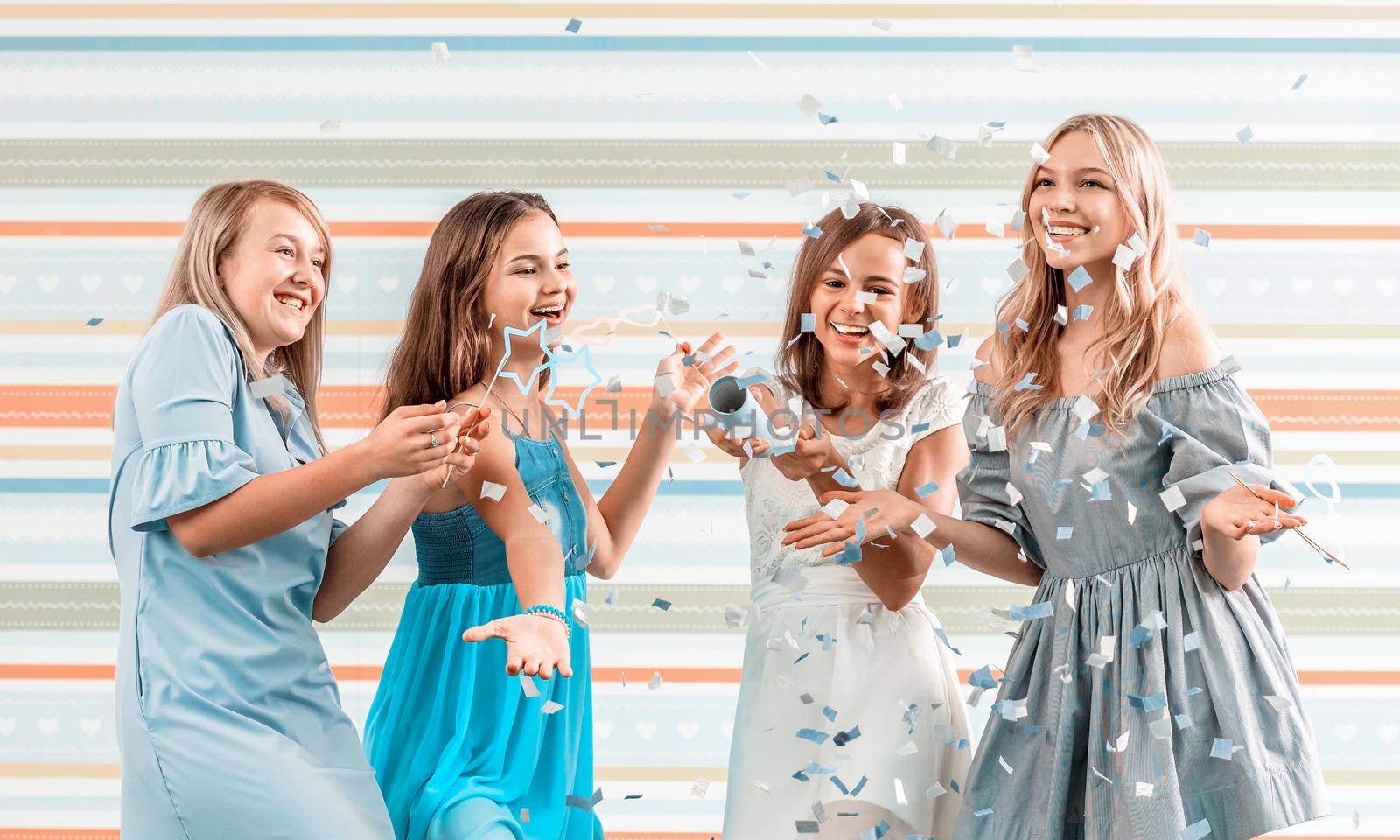 Smiling girls shoot confetti on striped background