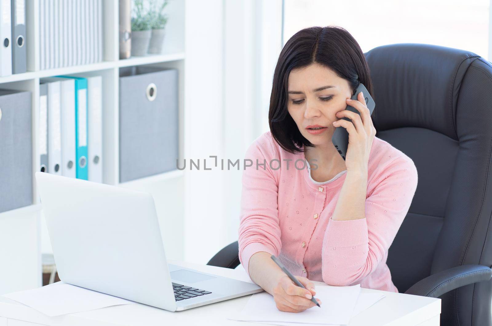 Pretty business woman talking on phone and making notes