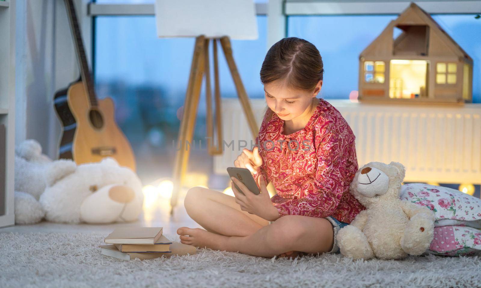 Little girl using smartphone sitting on floor in twilight room