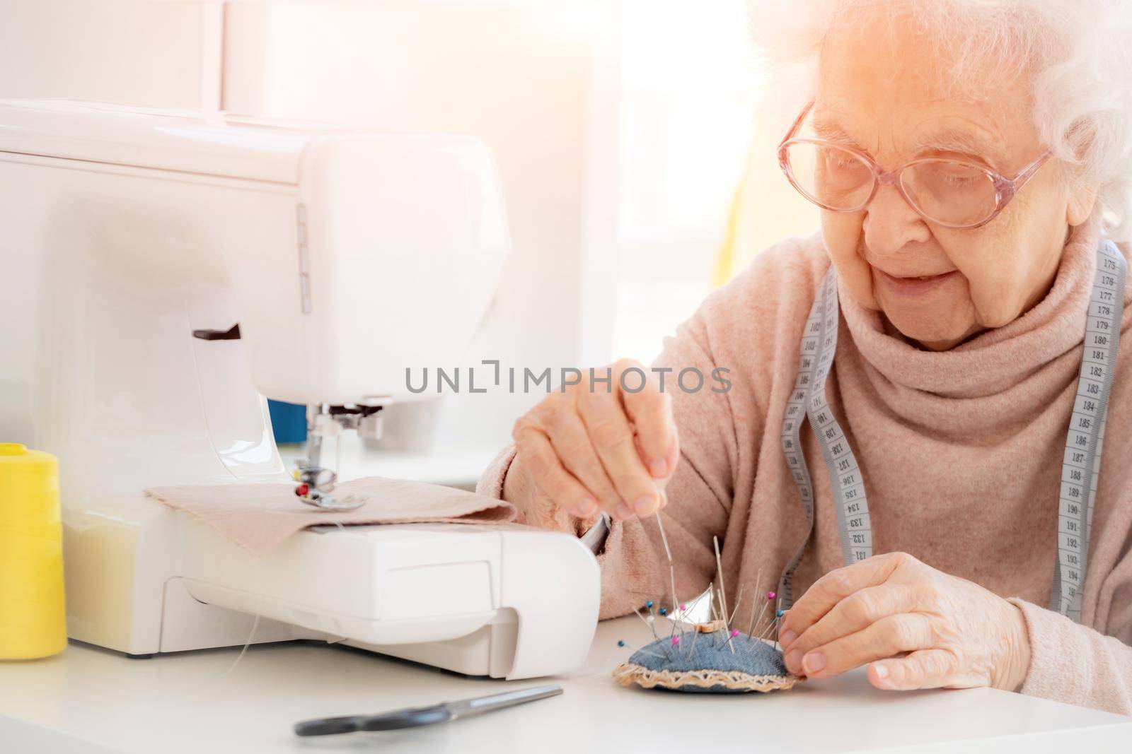 Lovely aged woman sewing at workshop