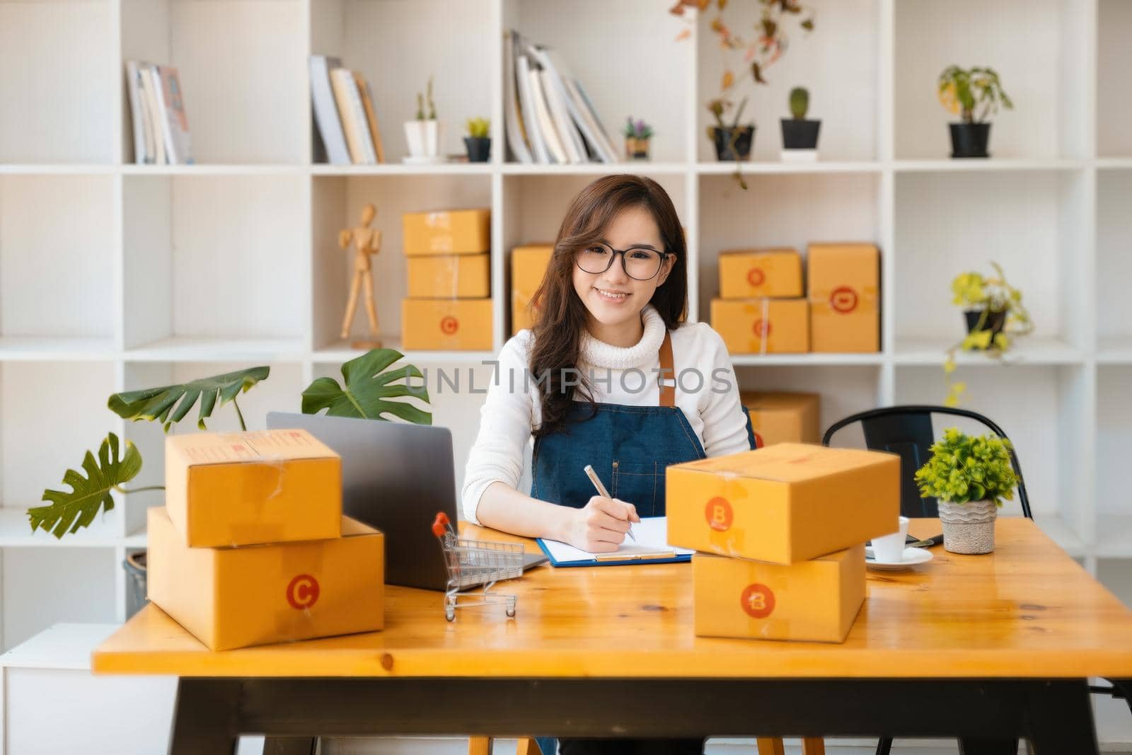 Entrepreneur owner using pen point note and laptop checking online purchase shopping order to preparing pack product box. Packing goods for delivery to customer. by Manastrong