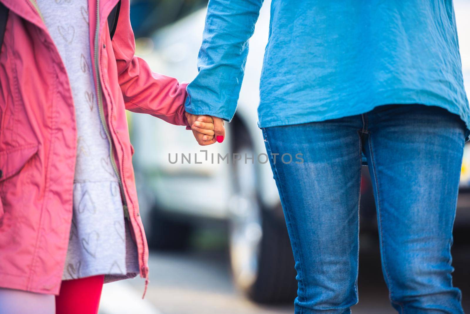 Little girl holding mother's hand on car background, close up