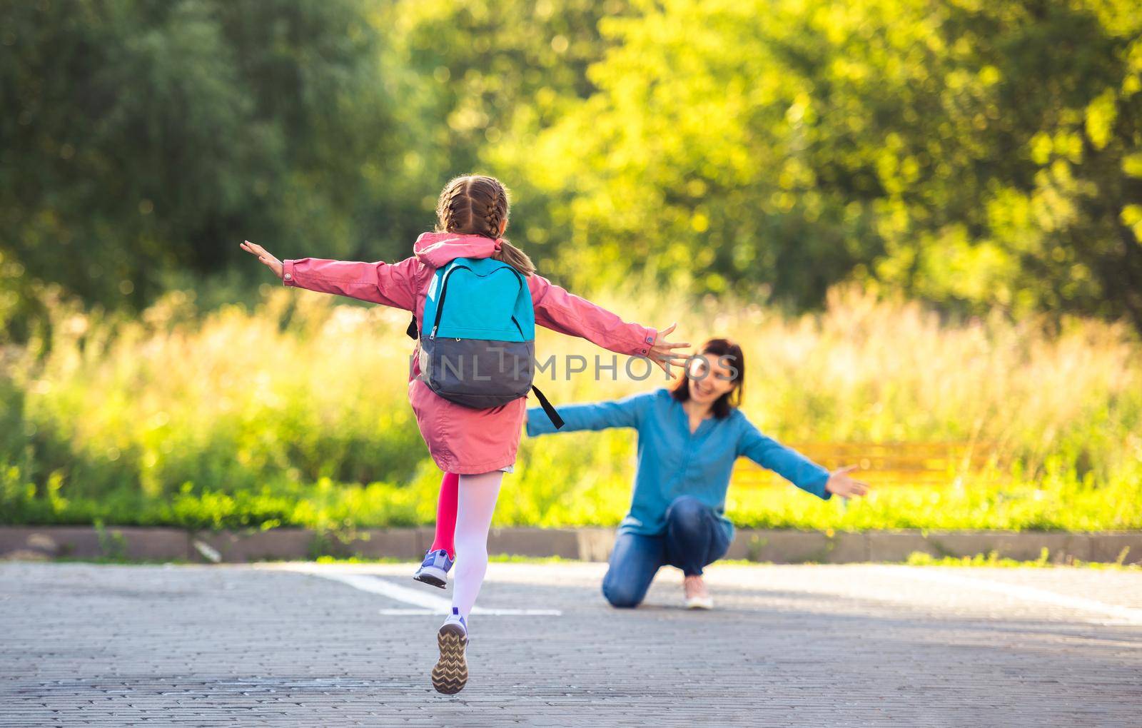 Back view of school girl running to mother after class on sunny street