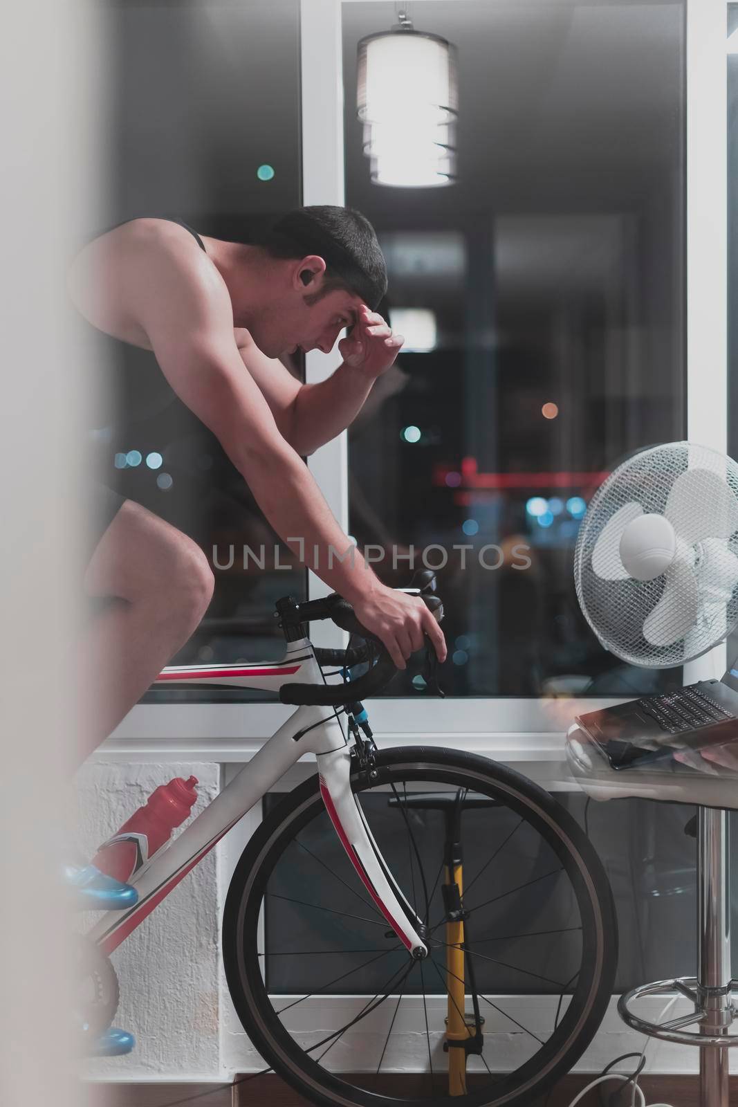 Man cycling on the machine trainer he is exercising in the home at night. Playing online bike racing game during coronavirus covid19 lockdown. New normal concept.