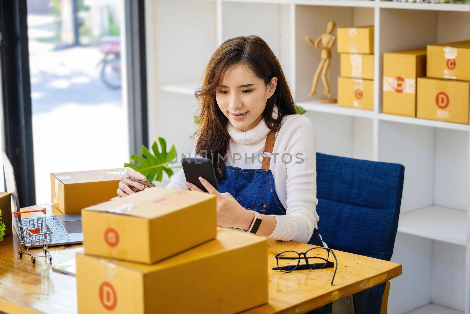 Work from home. happy women selling products online Start a small business owner by using smartphone and laptop computer to calculate prices and prepare for postage. by Manastrong