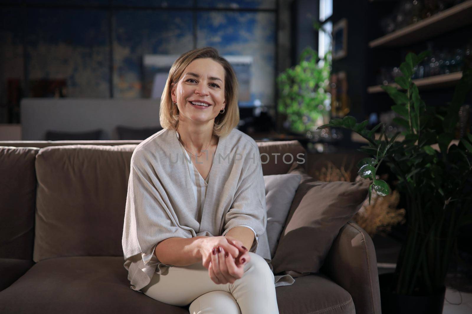 Beautiful blond middle aged woman relaxing sitting on sofa.
