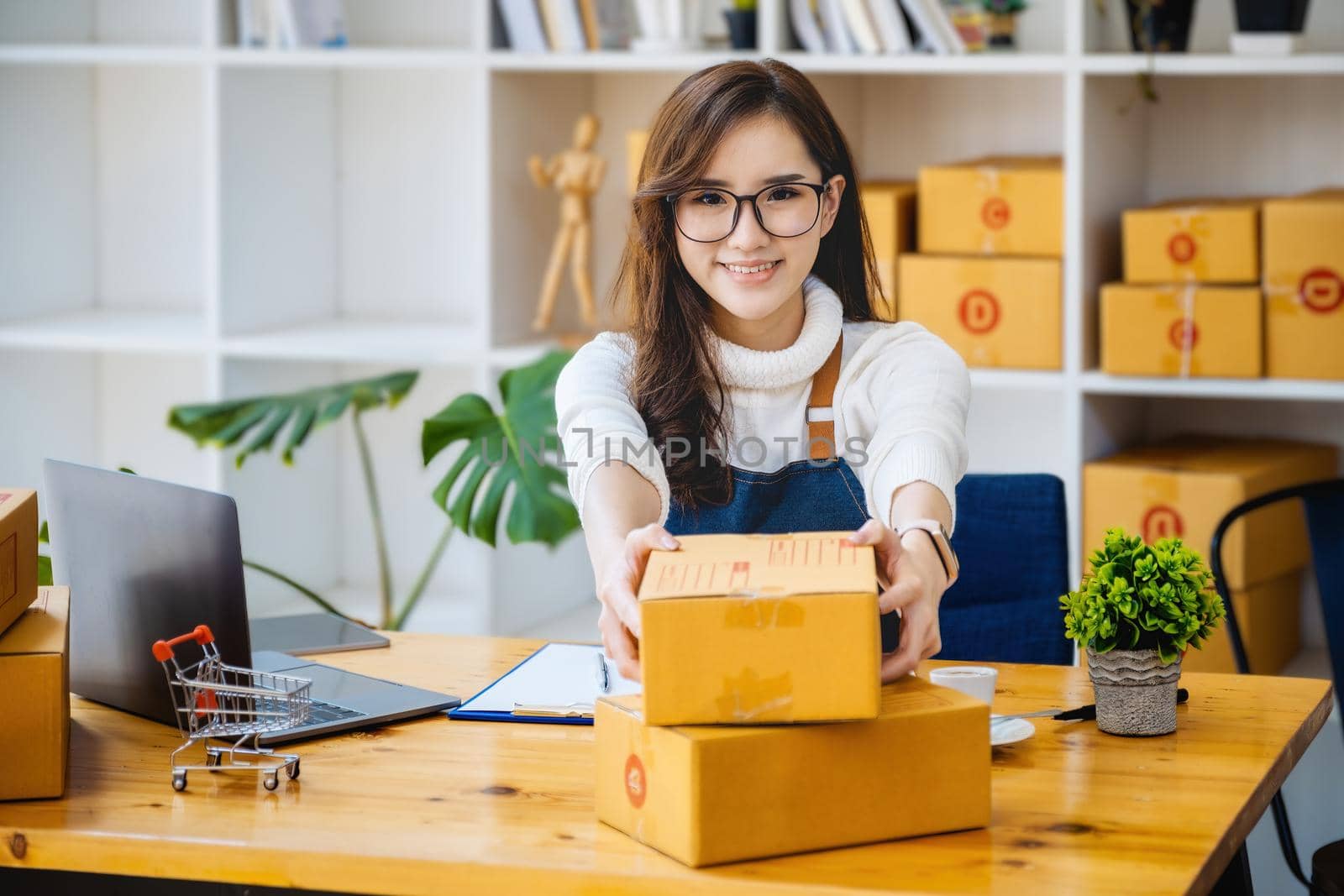 Business owner picking up parcel boxes And use a computer to check online orders to prepare the packaging. pack products to send to customers. by Manastrong