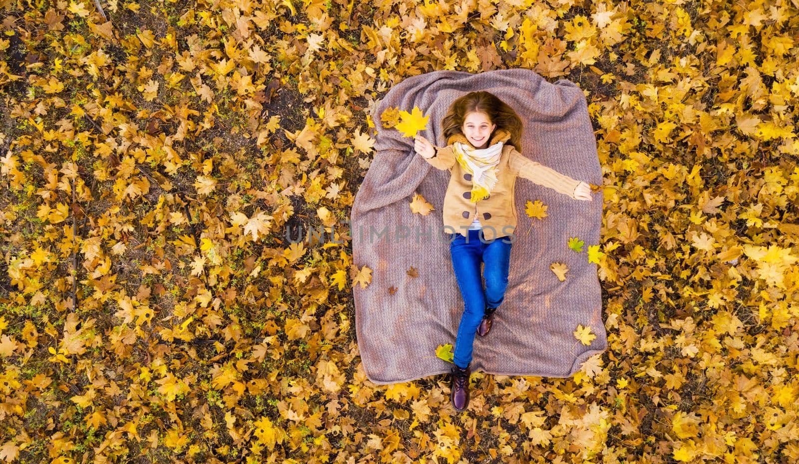 Nice girl lying on back surrounded by autumn leaves, view from above