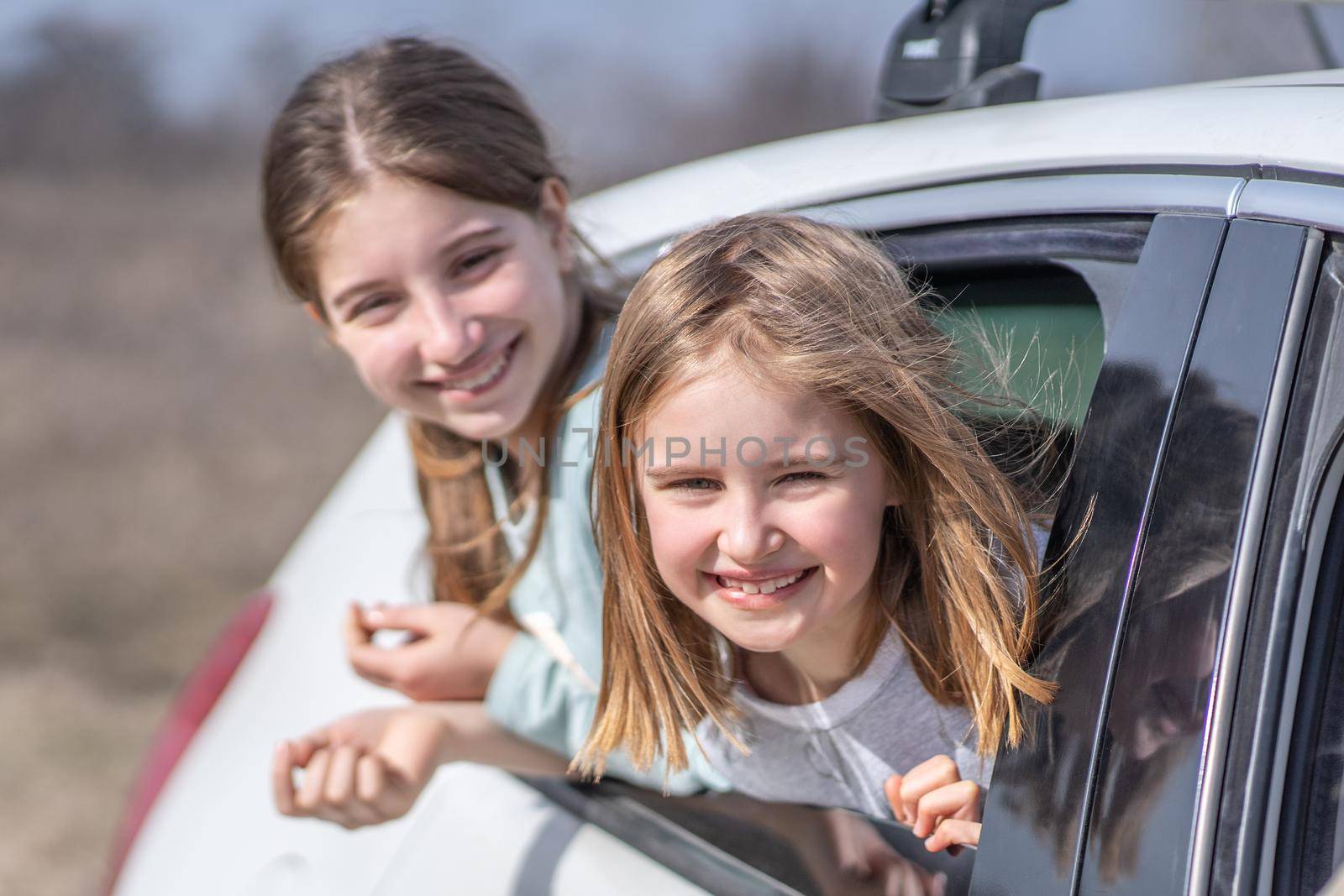 Happy girls looking out of car window at sunny day