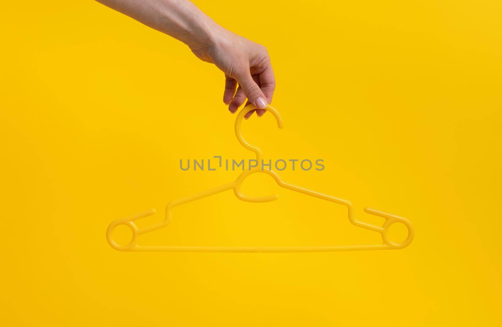 Hand holding hanger isolated on yellow horizontal background with copyspace. Stylish casual design look on fashion accessory. Concept of clothes retail