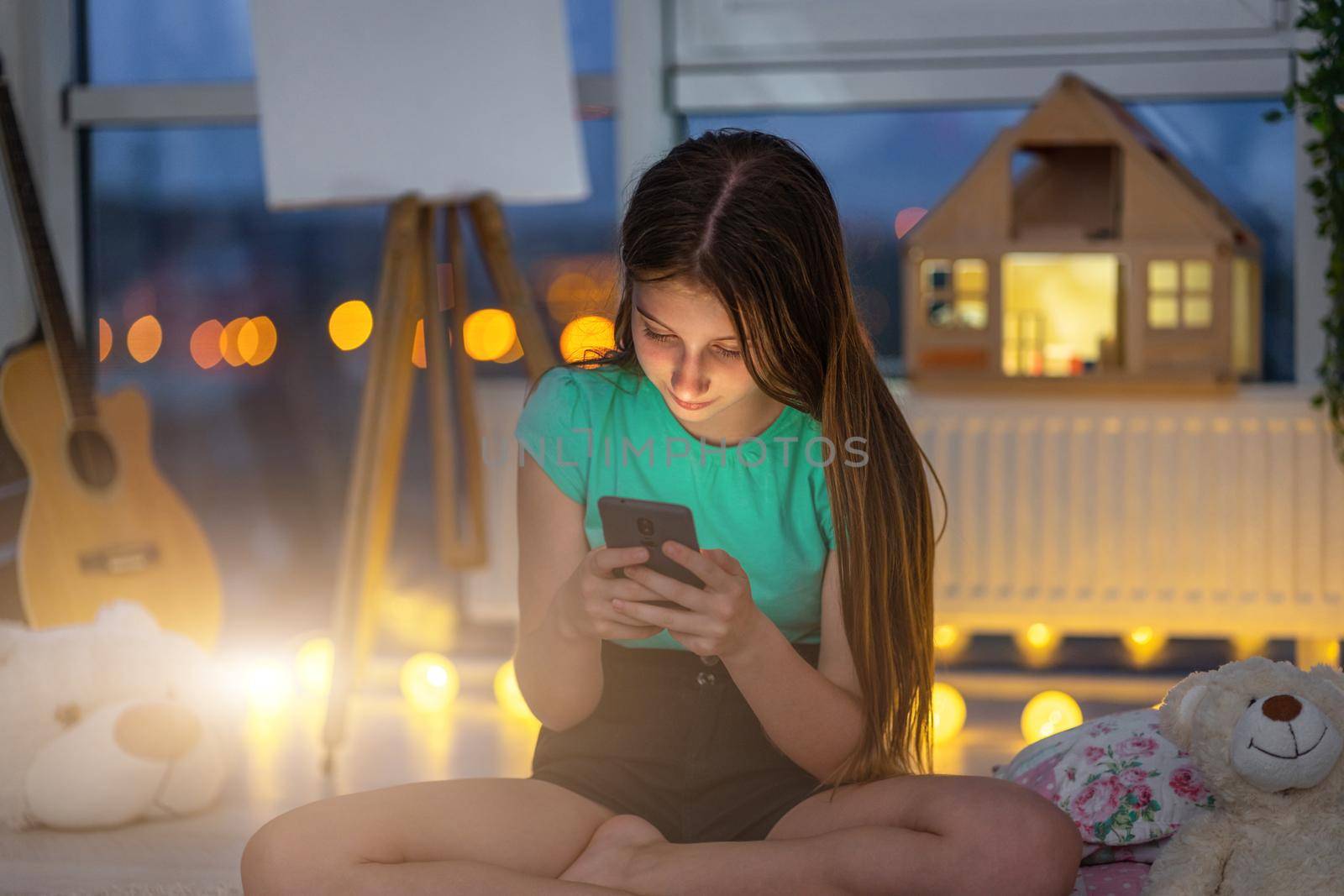 Young girl with smartphone sitting in twilight room