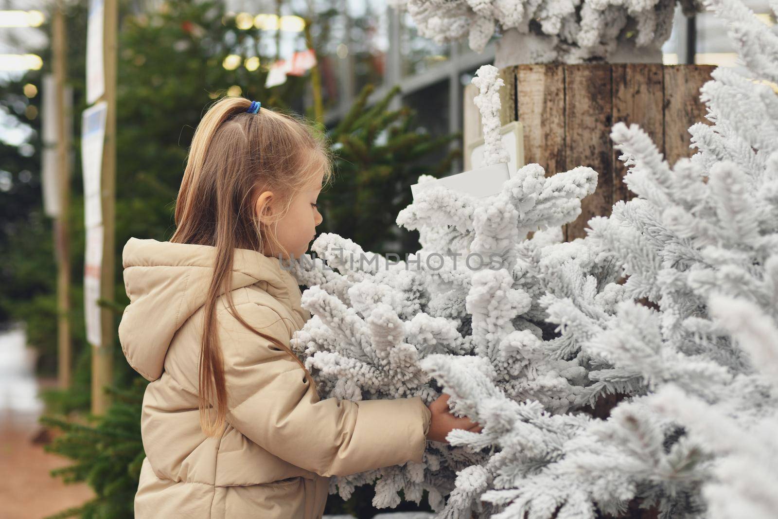 A girl and a white christmas artificial trees for sale on a shop