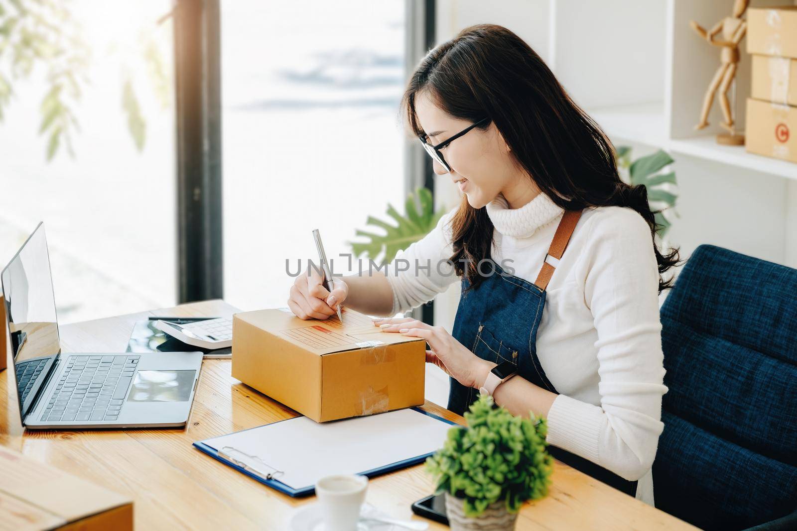 Business owners use pens to write on parcel boxes and use computers to check online orders to prepare packaged boxes. Pack products for delivery to customers. by Manastrong