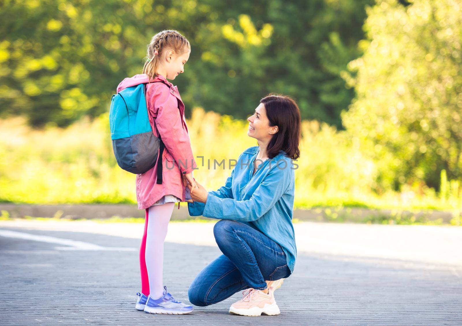 Schoolgirl with backpack saying goodbye to mother before class on parking
