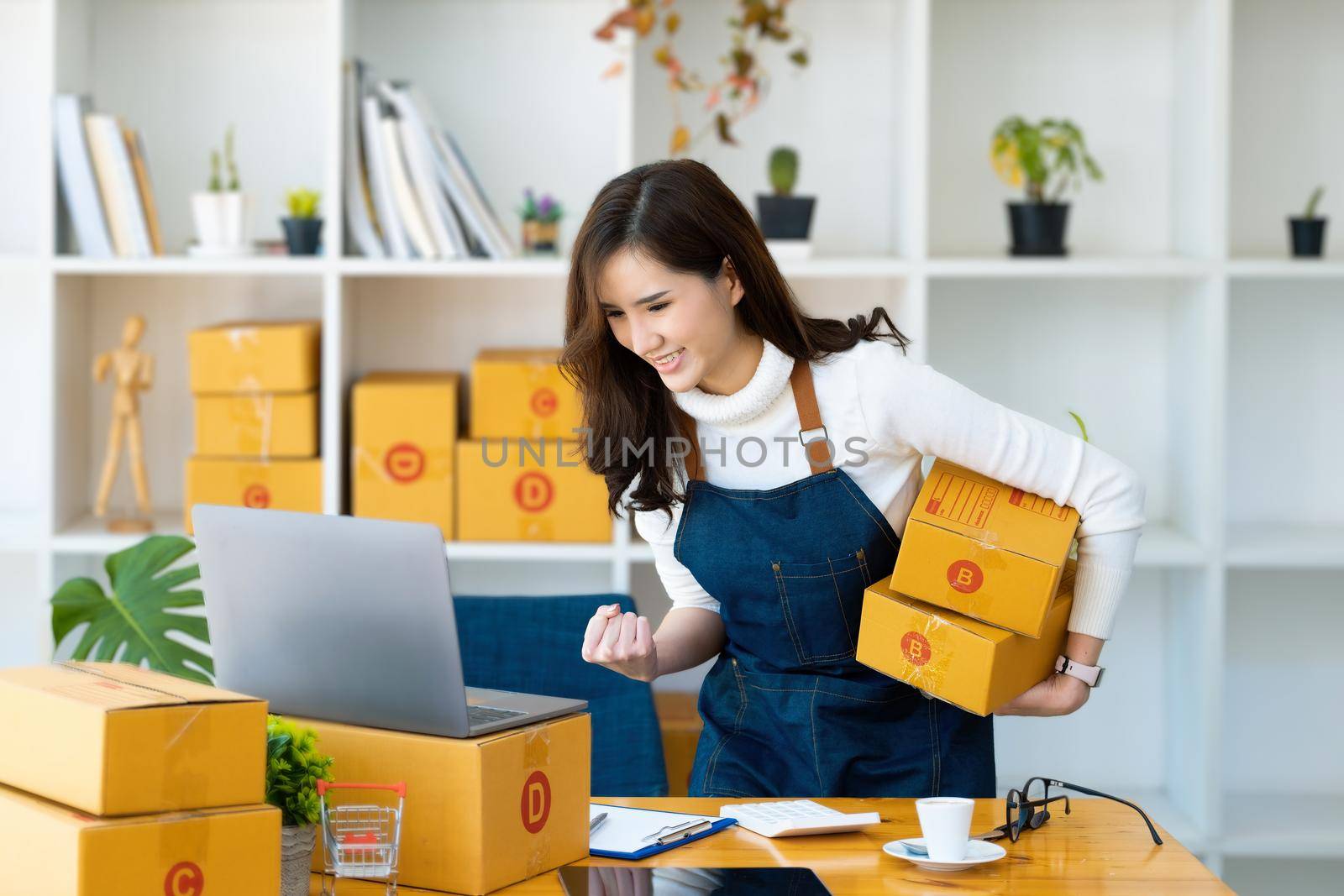 Work from home. happy women selling products online Start a small business owner by using laptop computer to calculate prices and prepare for postage. by Manastrong