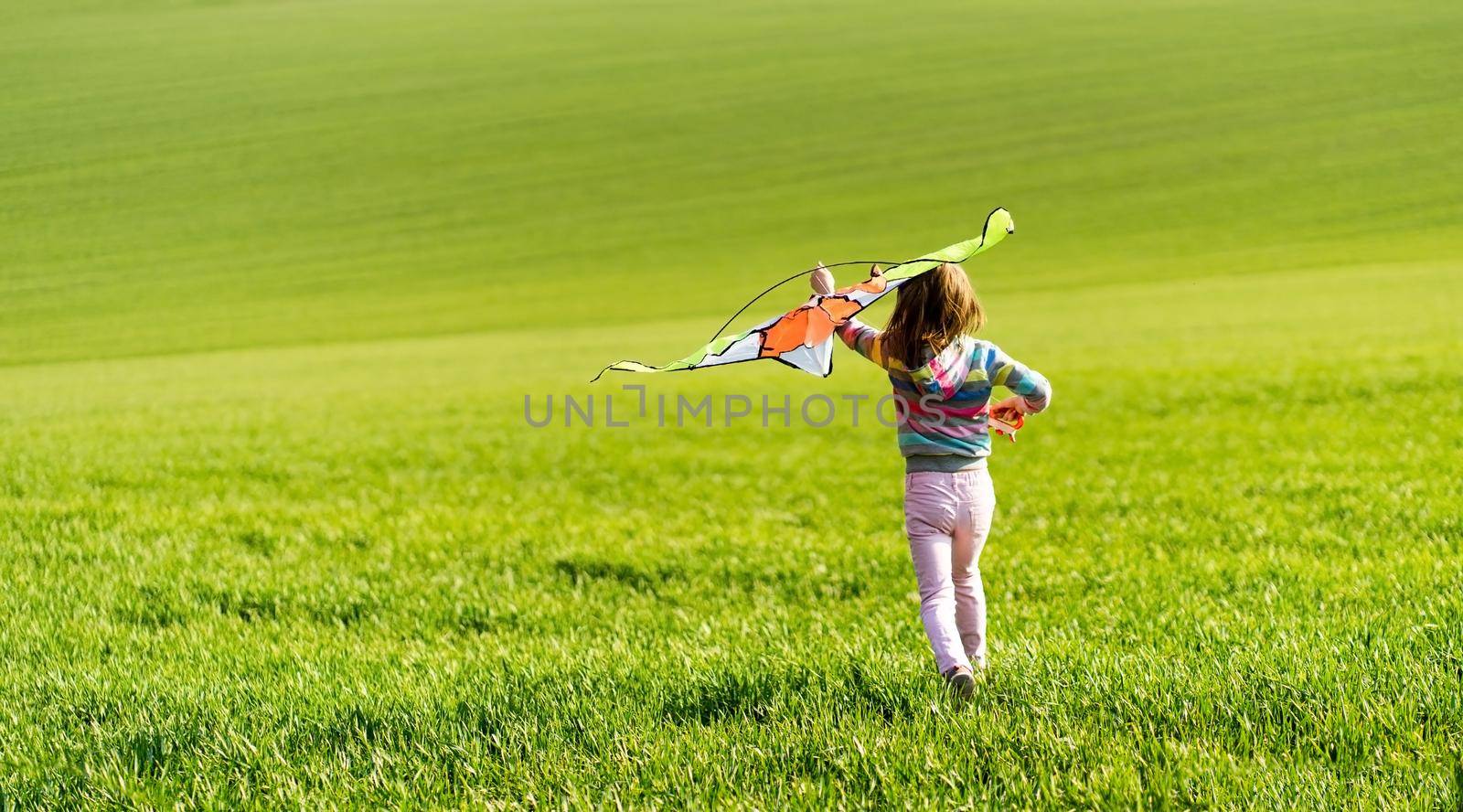 Little child girl running with kite on the field with green grass