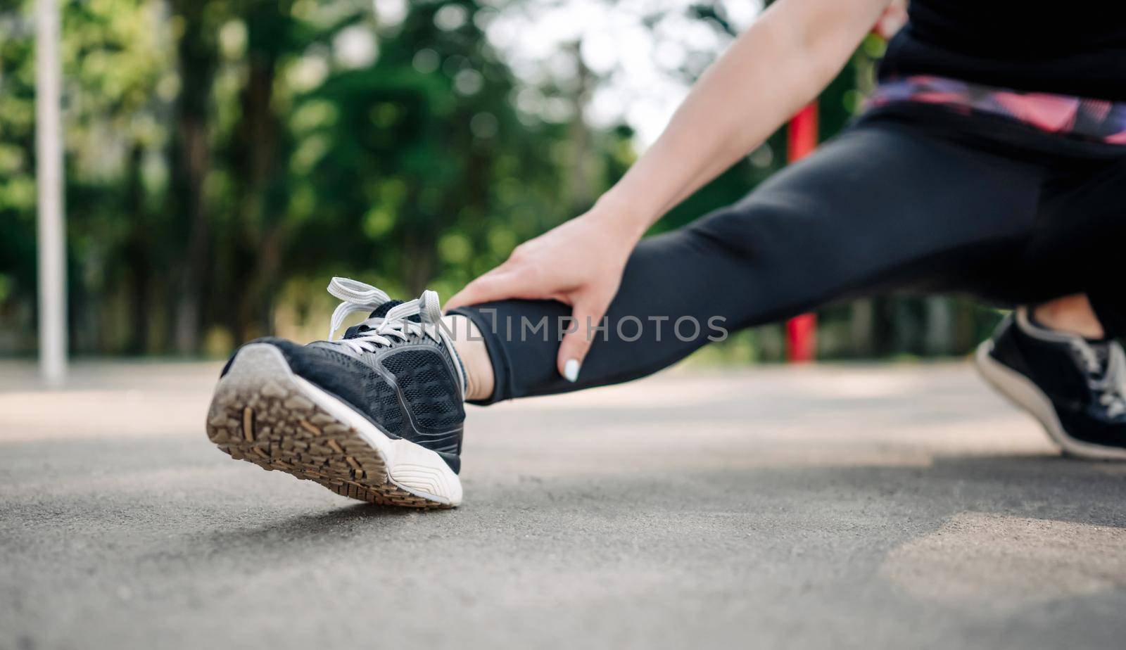 Young girl woman in sport outfit doing stretching outdoors preparing for active fitness workout. Closeup view on leg during training. Female sportsman exercising at stadium outside in the morning