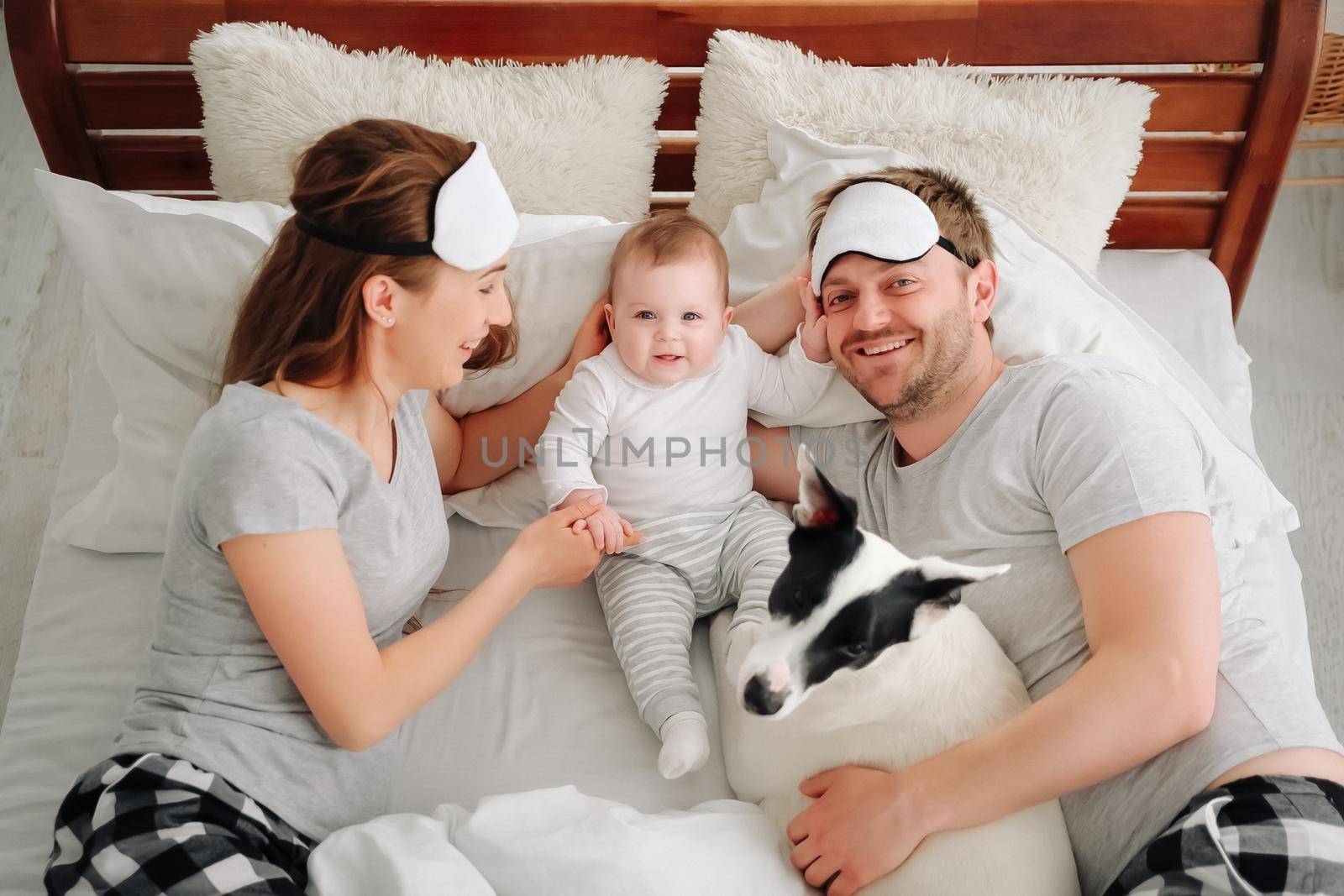 Family with child and dog lying in the bed together. Young mother and father resting with toddler kid and pet doggy in the morning