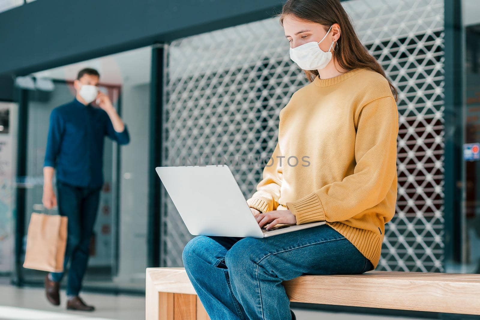 young woman is working on a laptop while sitting outside a city building. pandemic in the city