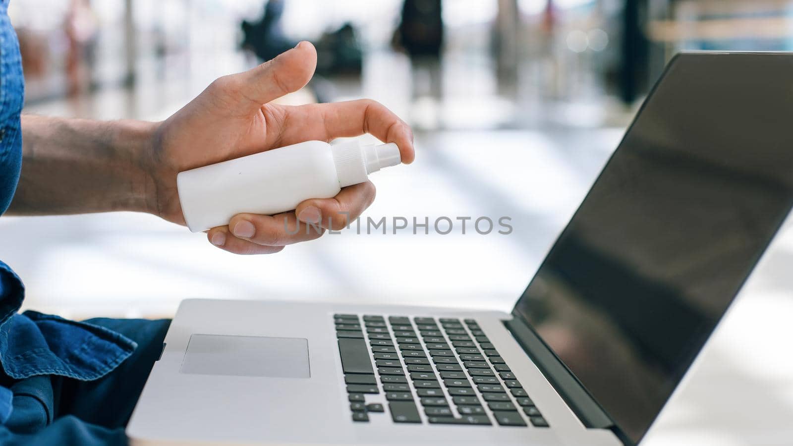 young man decontaminating his laptop with antiseptic. health protection concept