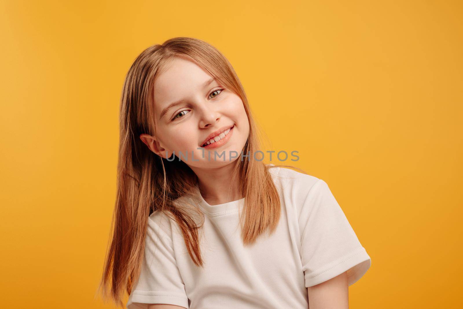 Beautiful little girl looking at the camera and smiling isolated on yellow background with copyspace. Cute teen kid portrait