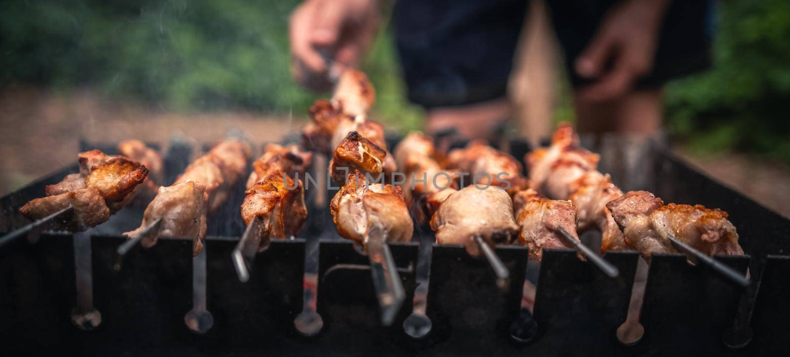 Man hand straightens the metal skewer with barbecue delicious grilled meat with smoke in the wood. Person preparing hot pork BBQ steaks at braizer