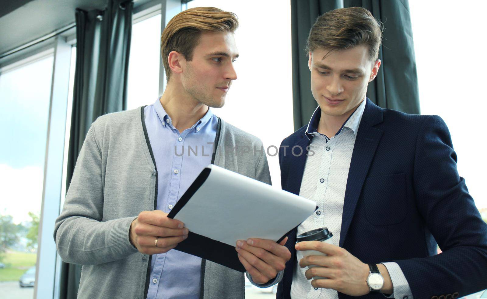 Two young modern men discussing work in the office